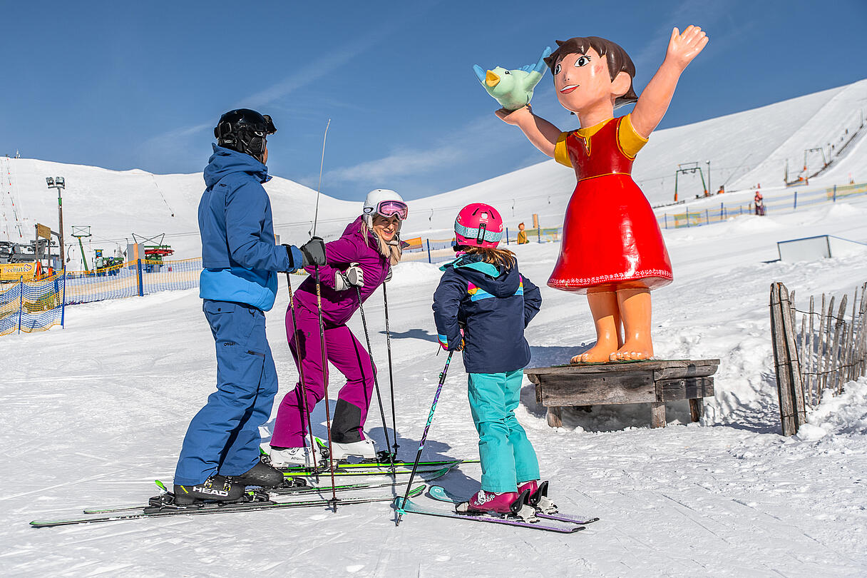 Skiurlaub mit Kindern im Heidi Alm Skipark Familie steht vor Heidifigur am Falkert